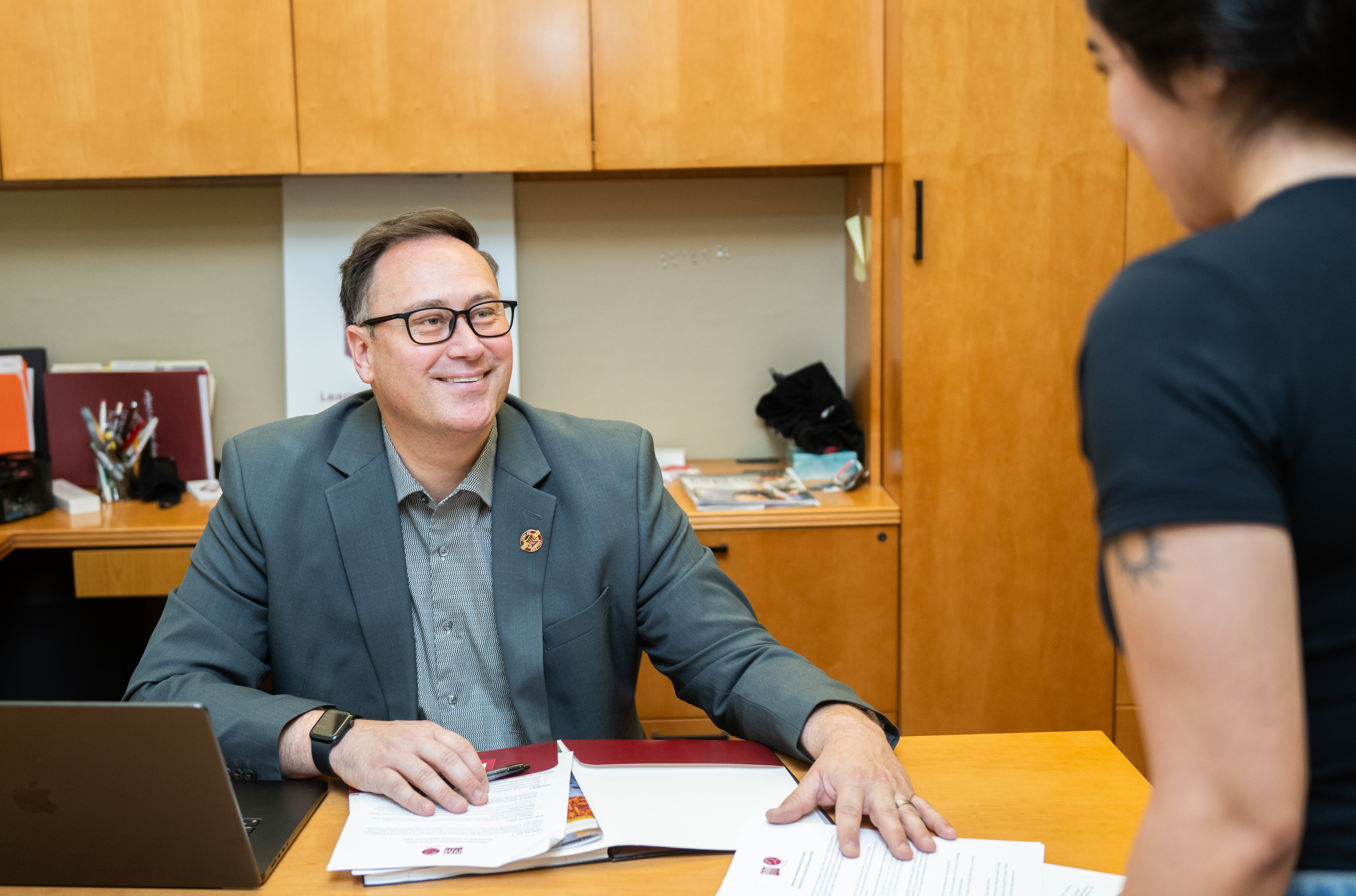 man smiling talking to student at desk 
